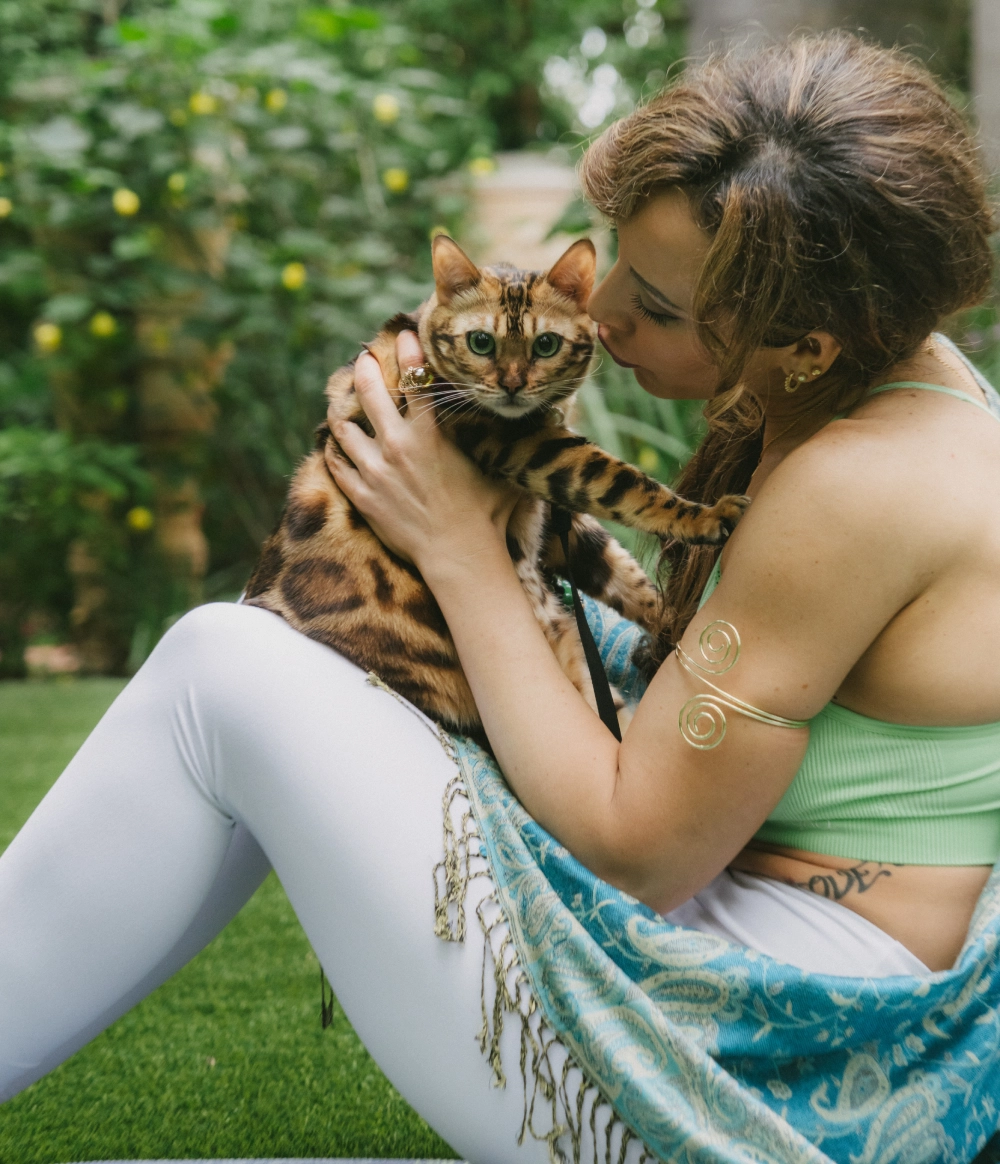 Woman cuddling a Bengal cat outdoors.